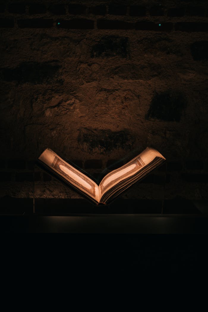 Dramatic photo of an illuminated open book against a rustic stone wall, exuding a vintage and sacred aura.