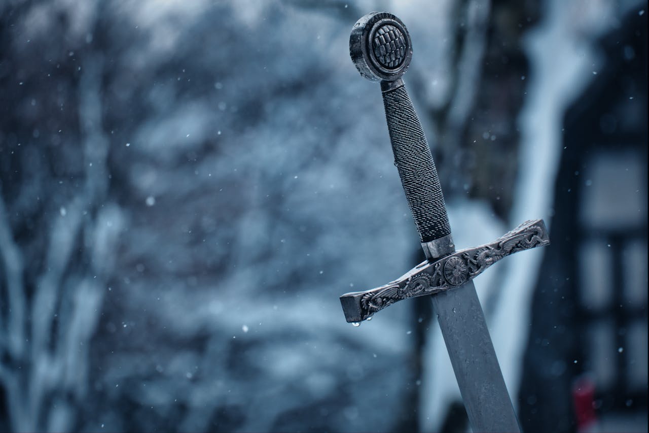 Close-up of a decorative medieval sword standing in a snowy outdoor setting.