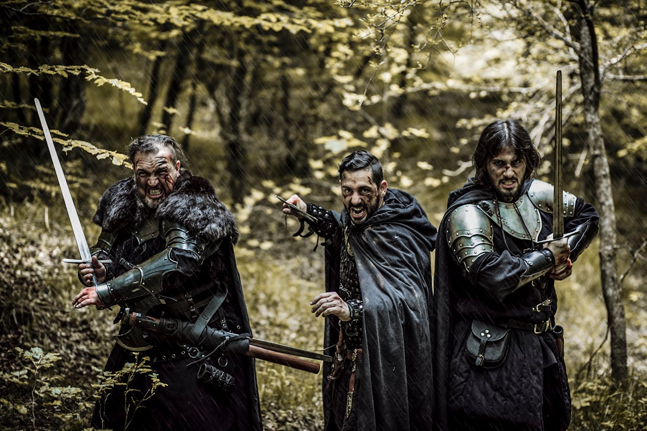 Three men in medieval armor and swords standing in a forest, ready for battle.